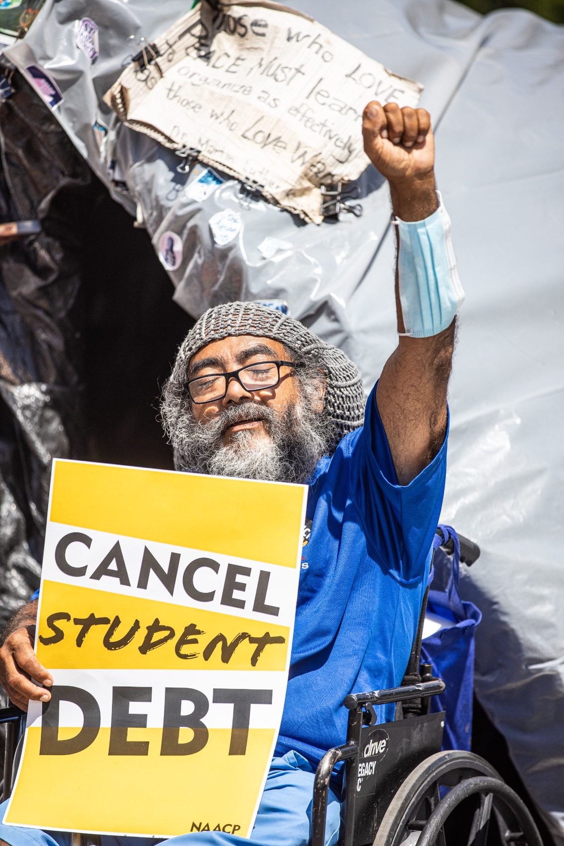 A demonstrator in a wheelchair holding a sign about student debt