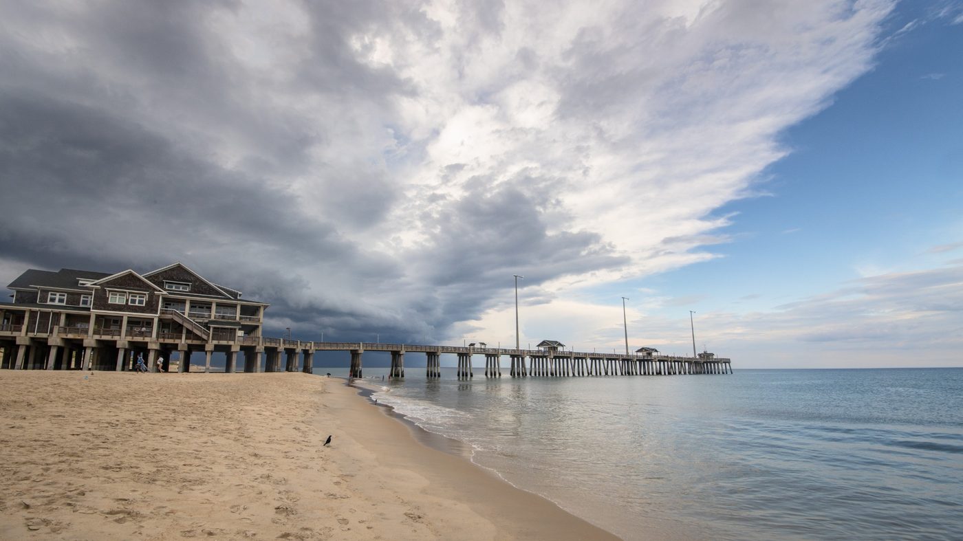 A long pier on the coast under dramatic storm clouds